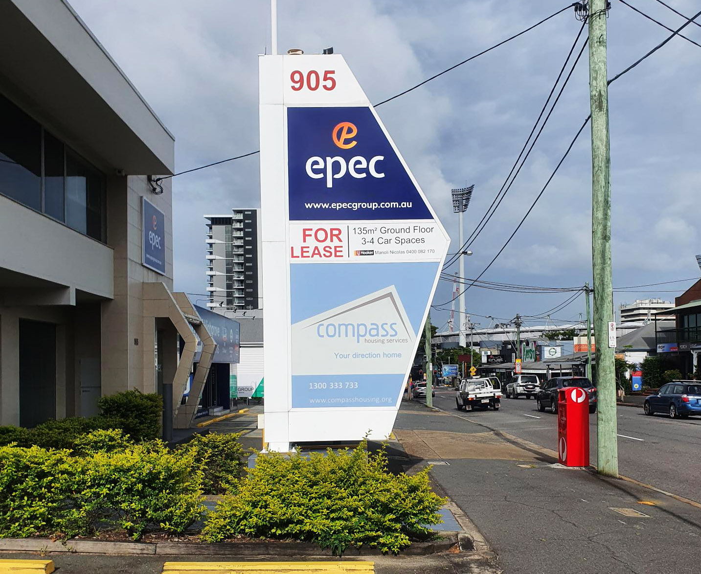A photo of the front of a building with a large pylon sign in front of the building, next to the sidewalk. Part of the sign pylon is a dark blue background with a white and orange logo that says EPEC.