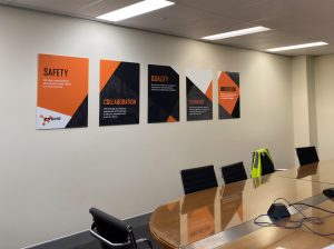 A photo of the inside of an office boardroom. There are five large, colourful orange and black posters on the wall.