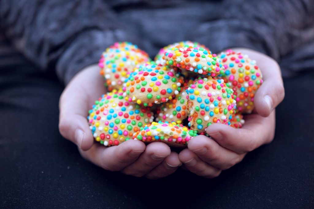 Hands holding a handful of rainbow sprinkle cookies